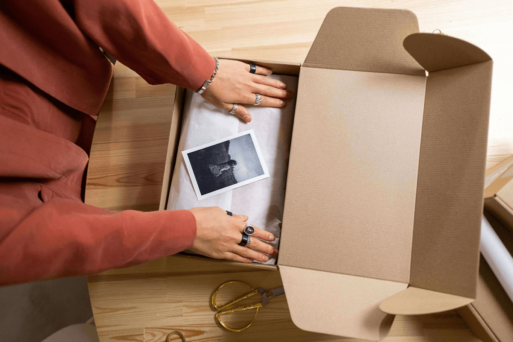 Hands opening ecommerce packaging with custom tissue paper and printed card, highlighting the unboxing experience as a brand's first physical impression.