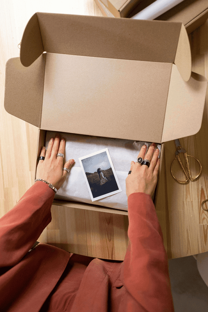 Hands opening ecommerce packaging with custom tissue paper and printed card, highlighting the unboxing experience as a brand's first physical impression.