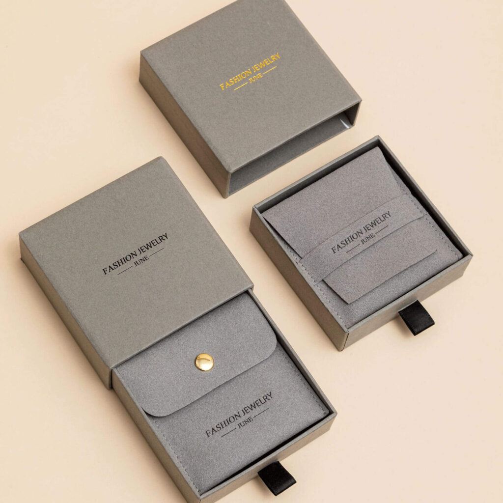 Luxury jewelry packaging bags in soft grey fabric with button and flap closure, featuring minimalist custom branding for premium jewelry presentation.