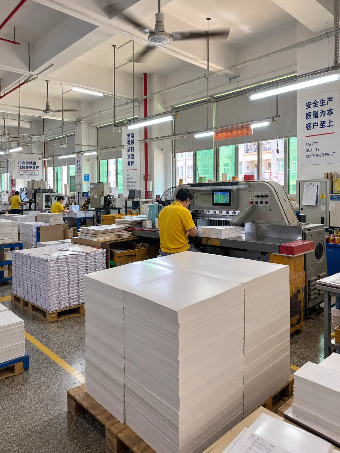 Custom paper packaging factory in Fujian, China, with industrial paper cutting equipment, production workers, and stacked paperboard ready for packaging production.